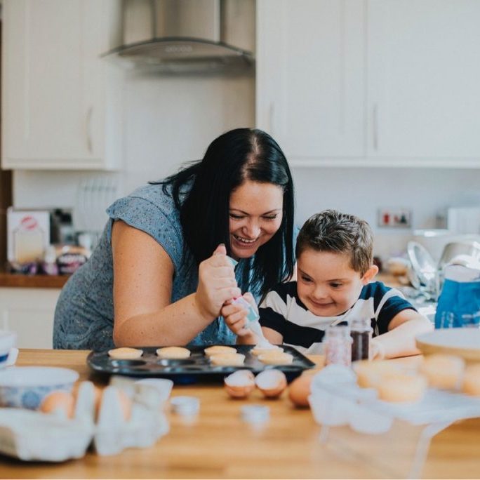 enfant en situation de handicap qui apprend à faire la cuisine avec une garde d'enfant